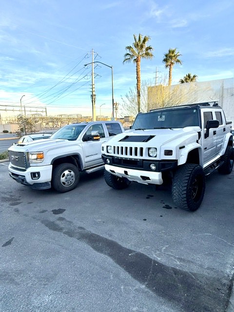 A lifted Hummer H2 SUT beside a GMC Sierra Denali HD in the shop lot.