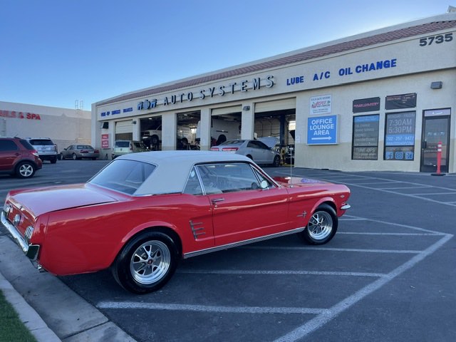 A red 1966 Ford Mustang convertible parked in front of the R&R Auto Systems bays.